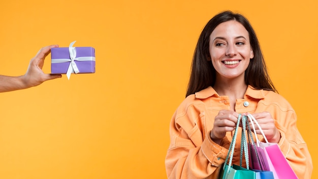 Smiley-Frau, die Einkaufstaschen hält und Geschenk betrachtet, das sie angeboten wird