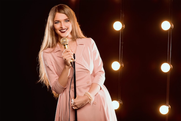 Smiley hermosa mujer con micrófono cantando canciones en el escenario de karaoke