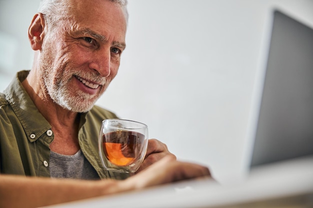 Smiley jubilado tomando té y revisando su computadora portátil