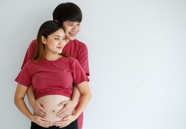 Smiley junger Mann und Frau stehen zusammen über weißem Hintergrund. Ein Mann umarmt eine schwangere Frau und legt seine Hand auf ihren Bauch. Menschen, Familie und Lifestyle-Konzept. Platz kopieren.