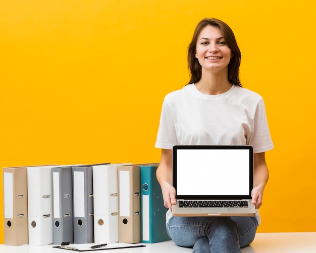 Foto smiley mulher sentada na mesa e segurando laptop