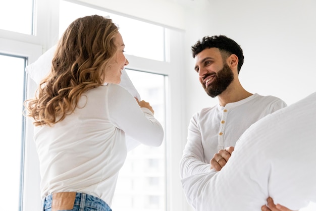 Foto smiley pareja lucha de almohadas en casa