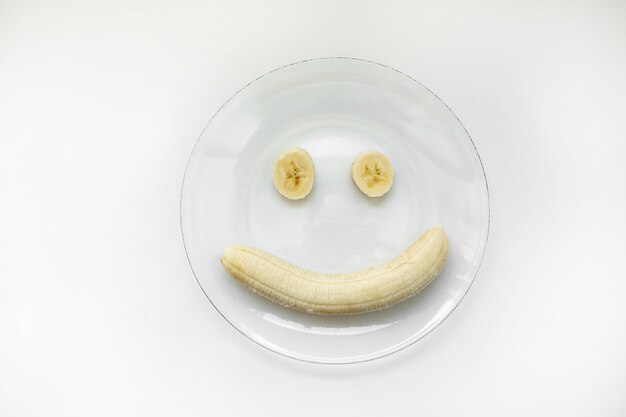 Smiley de plátano y rodajas en un plato sobre un fondo blanco.