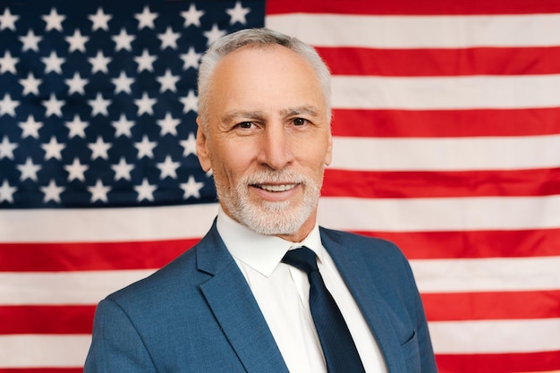 Foto smiling senior bearded gray haired man presidential candidate wearing suit posing on american flag