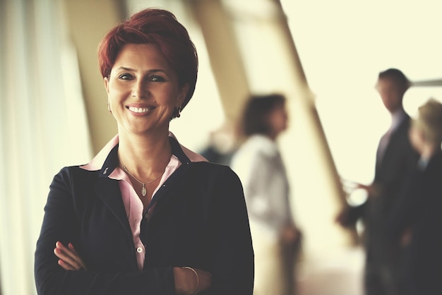 Smilling jovem mulher de negócios na frente de sua equipe blured no fundo. Grupo de jovens empresários. Interior moderno do escritório de inicialização brilhante.