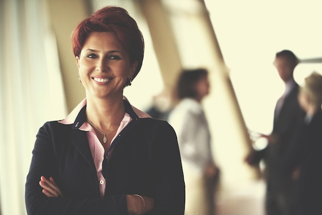 Smilling jovem mulher de negócios na frente de sua equipe blured no fundo. grupo de jovens empresários. interior moderno do escritório de inicialização brilhante.