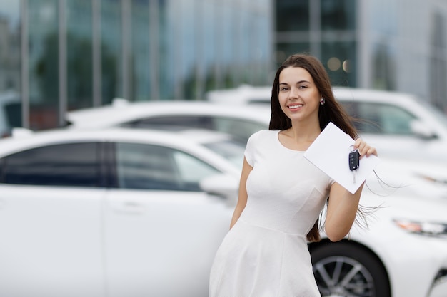 Smilling mujer con llaves y acuerdo sobre antecedentes de concesionario de automóviles