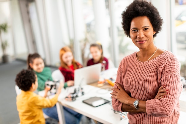 Smily profesora de ciencias afroamericana con un grupo de niños que programan juguetes eléctricos