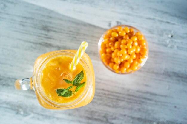 Smoothie amarelo orgânico fresco na caneca de vidro na mesa de madeira branca close-up refrescante bebida de frutas de verão o conceito de alimentação saudável smoothie de espinheiro mar