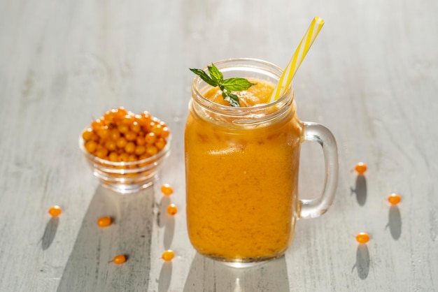 Smoothie amarelo orgânico fresco na caneca de vidro na mesa de madeira branca close-up Refrescante bebida de frutas de verão O conceito de alimentação saudável Smoothie de espinheiro mar