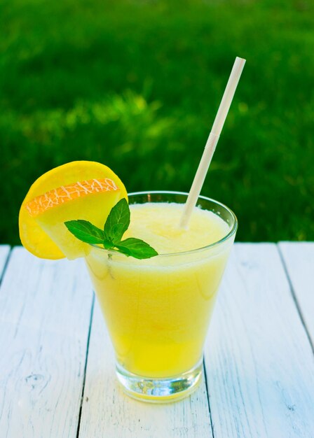 Smoothie brilhante feito de melão com hortelã e limão em um fundo de grama verde fresca