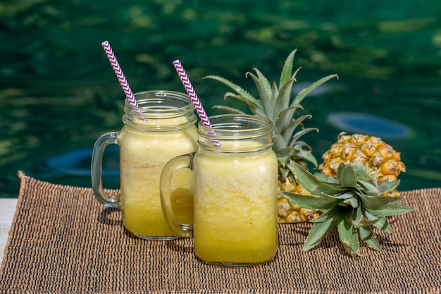 Smoothie caseiro de manga e abacaxi feito com leite de coco em duas canecas de vidro perto da piscina Ilha Bali Indonésia Refrescante bebida de frutas tropicais