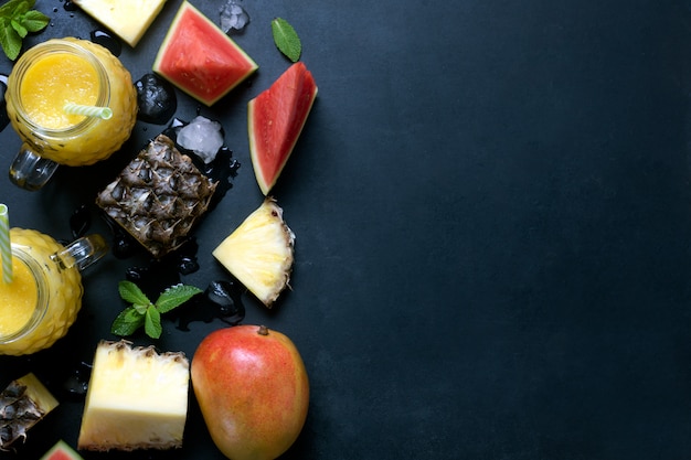 Smoothie de abacaxi e manga fresca em copos com frutas em um fundo preto rústico