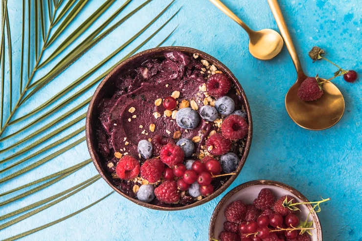 Smoothie de açaí congelado em casca de coco com framboesas, banana, mirtilos, frutas e granola no fundo de concreto. Café da manhã, refeição saudável para vibrações de verão, vista de cima, espaço para texto