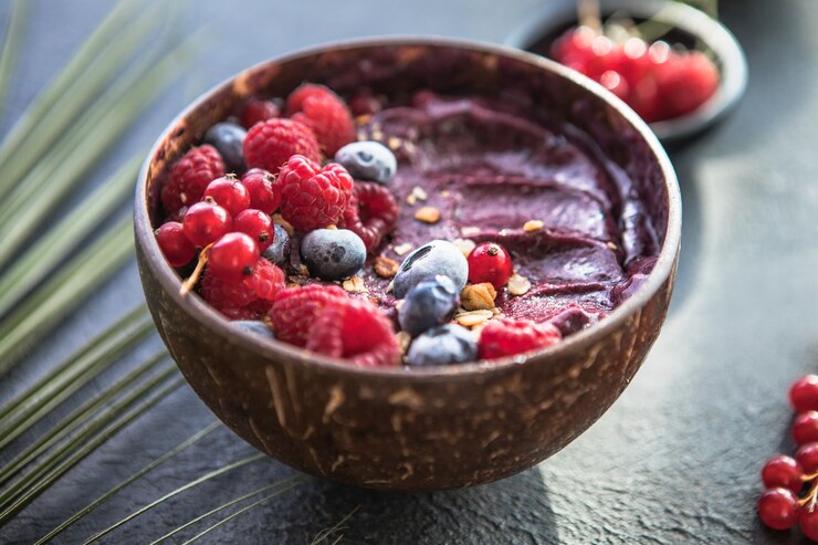 Foto smoothie de açaí congelado em casca de coco com framboesas, banana, mirtilos, frutas e granola no fundo de concreto. café da manhã, refeição saudável para vibrações de verão, vista de cima, espaço para texto