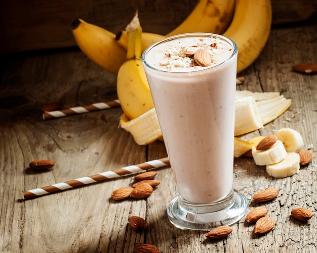 Smoothie de banana com amêndoas moídas de leite em um copo grande na velha mesa de madeira foco seletivo