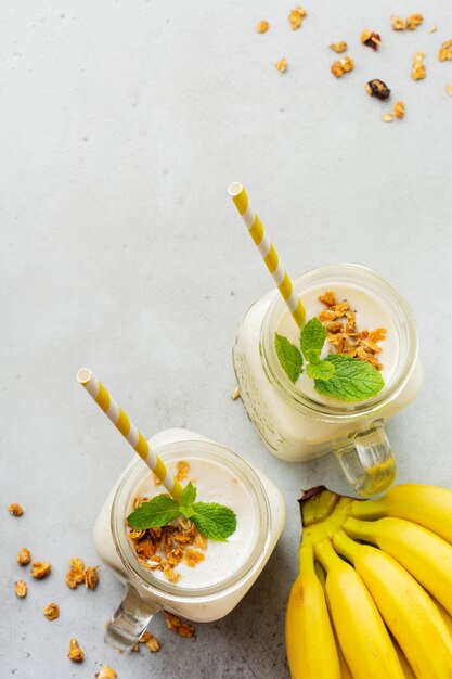 Smoothie de banana com granola, frutas secas e hortelã na superfície de concreto cinza