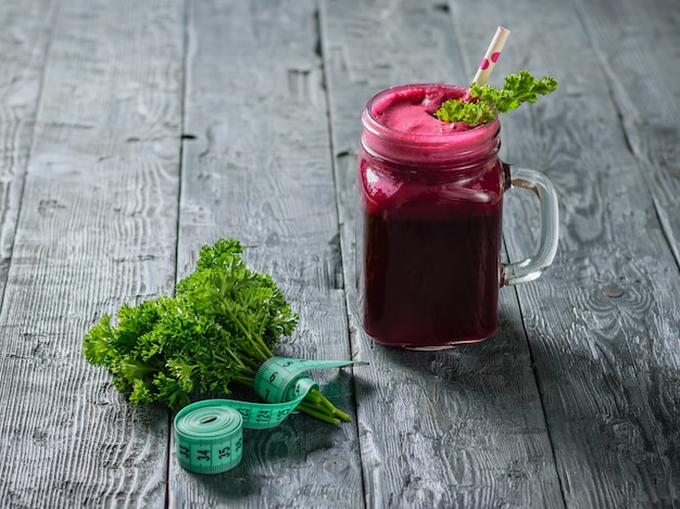 Smoothie de beterraba fresca, fita métrica, duas beterrabas e salsa na mesa de madeira preta