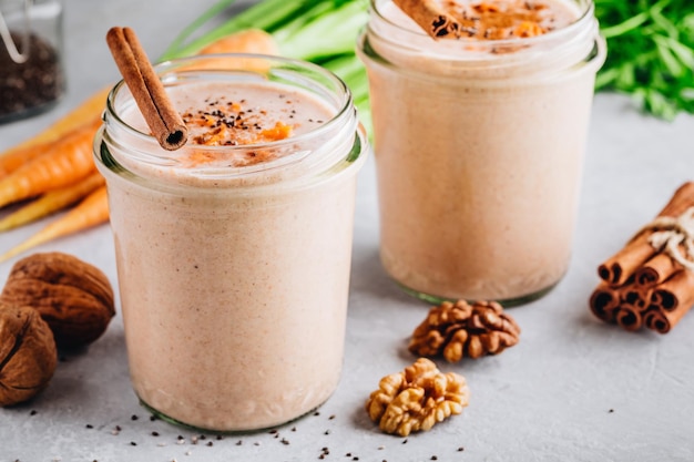 Smoothie de bolo de cenoura saudável com nozes, canela e sementes de chia em frascos de vidro sobre fundo de pedra cinza