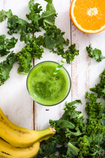 Smoothie de couve com banana e laranja em fundo branco de madeira