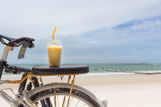 Smoothie de fruta fresca fria na bicicleta contra a praia de areia branca contra o mar. Conceito de férias.