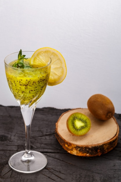 Smoothie de kiwi decorado com hortelã e limão em um copo em um fundo preto perto de kiwi