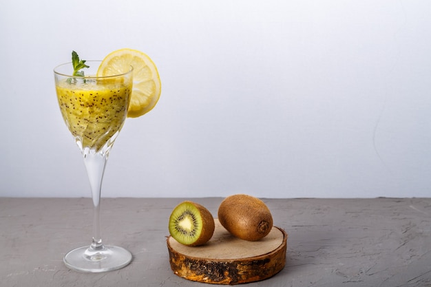 Smoothie de kiwi decorado com hortelã e limão em um copo em uma superfície cinza perto de kiwi