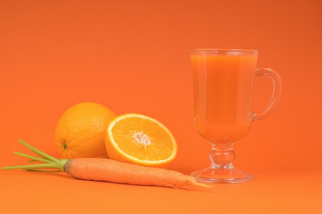 Smoothie de laranja e cenoura em um copo de vidro em um fundo laranja. o conceito de alimentação saudável.