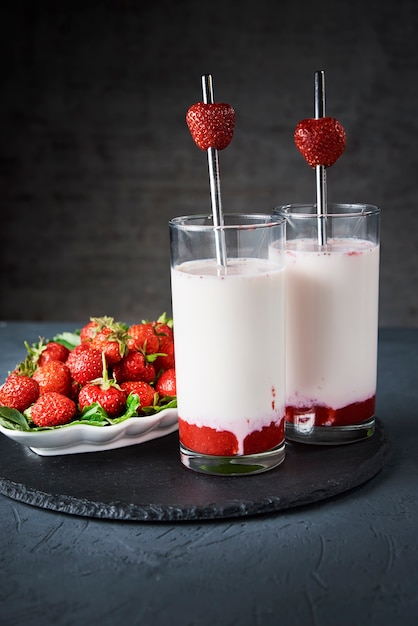 Smoothie de leite de morango em copo com palha e frutas frescas em fundo escuro