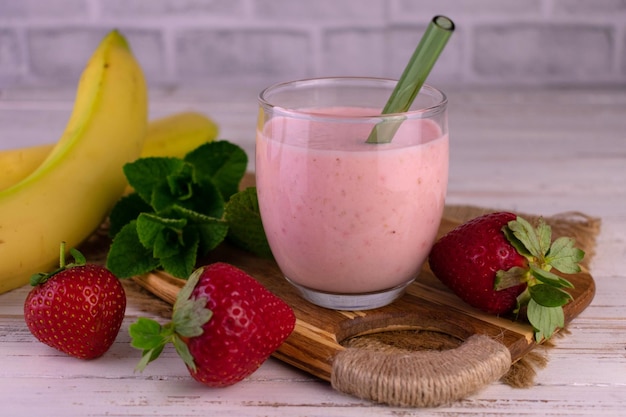 Smoothie de morango e banana em um copo em uma placa de madeira