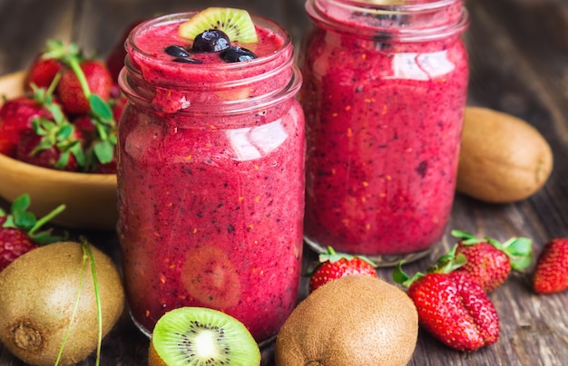 Smoothie mit Erdbeerkiwi und Blaubeeren in Gläsern auf rustikalem Holzhintergrund