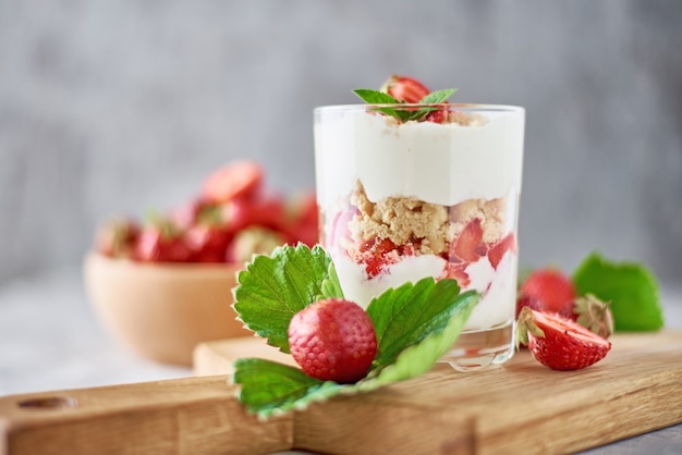 Smoothie mit Sommererdbeere im Glasgefäß und frischen Beeren in der hölzernen Schüssel auf einem Grau