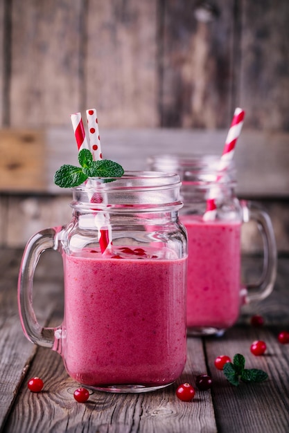 Smoothie rosa com cranberries selvagens em frasco de pedreiro com hortelã e palha em fundo de madeira rústica