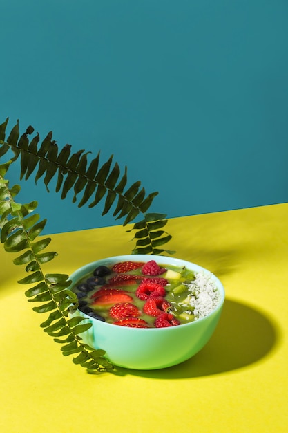 Smoothie-Schüssel mit frischen Beeren und Früchten in blauer Platte auf hochwertigem Foto des gelben dunklen Schattens