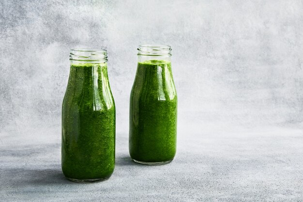 Smoothie verde com espinafre em pequenas garrafas no conceito de comida saudável espaço de cópia de fundo cinza