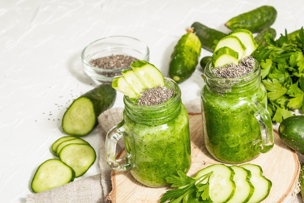 Smoothie verde com pepino em uma jarra de vidro. Legumes frescos maduros, verduras e sementes de chia. Luz dura na moda, sombra escura. Fundo de massa branca, close-up