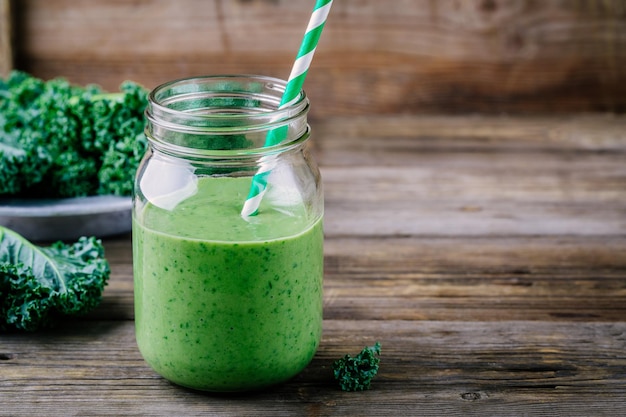 Smoothie verde de desintoxicação saudável com couve em frasco de pedreiro em fundo de madeira rústica