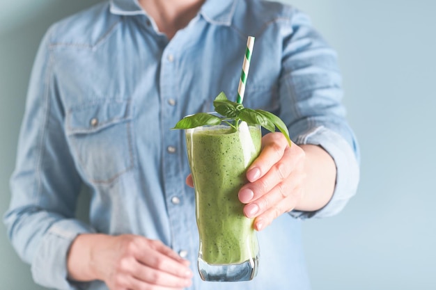 Smoothie verde de espinafre Smoothie vegano de sementes de chia de manjericão verde espinafre e hortelã em vidro nas mãos de uma mulher em fundo azul Comer limpo dieta alcalina conceito de comida para perda de peso Mock up