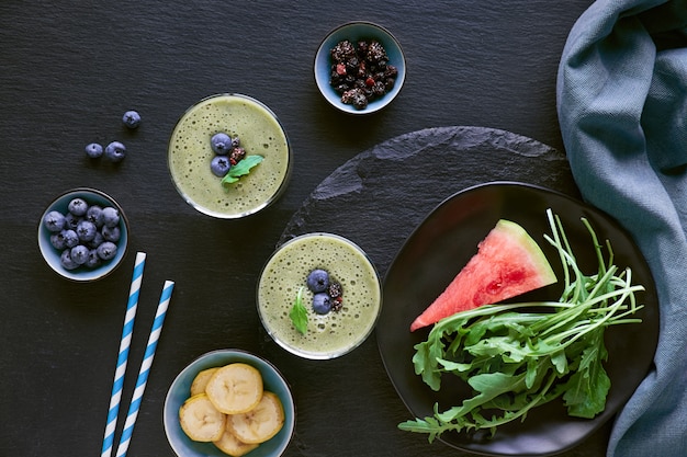 Smoothie verde de rúcula, banana e melancia em potes de vidro na mesa de ardósia escura