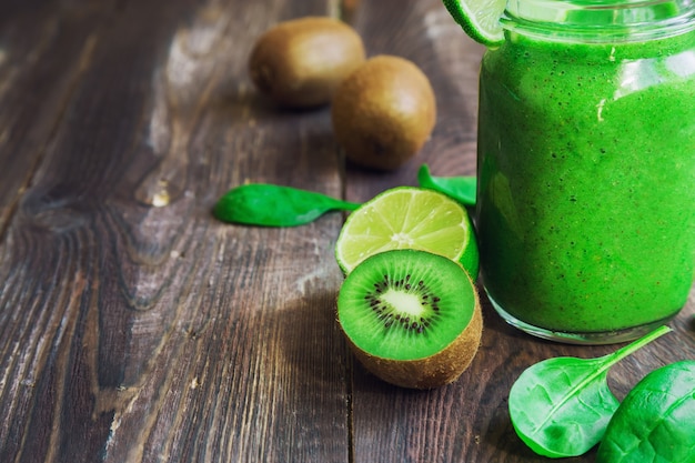 Smoothie verde fresco com kiwi, limão e espinafre em fundo de madeira rústico