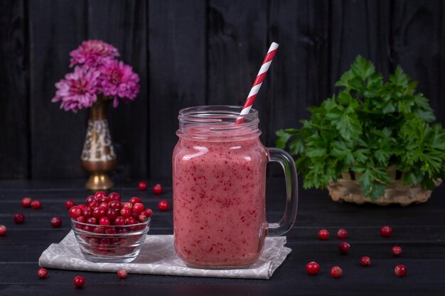 Foto smoothie vermelho orgânico fresco na caneca de vidro na mesa de madeira preta, close-up. bebida refrescante de frutas de verão. o conceito de alimentação saudável. smoothie de cranberry e framboesa