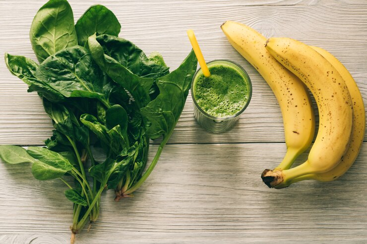 Smoothies com uma palha, uma banana e folhas de espinafre no fundo de madeira branco