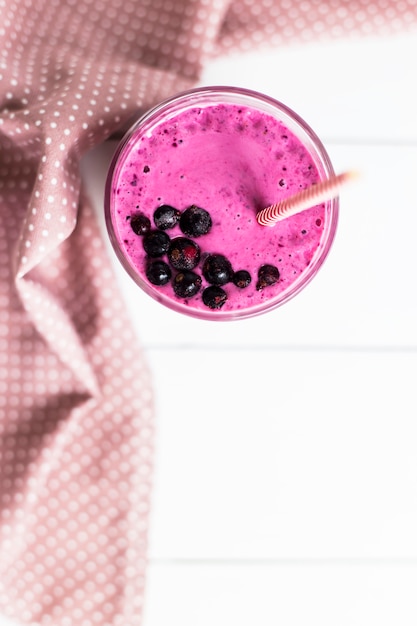 Smoothies de banana groselha em um copo sobre uma mesa branca ao lado de um guardanapo rosa em manchas com um canudo