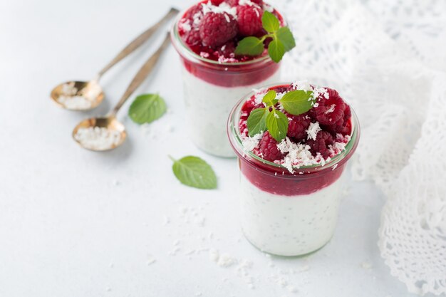 Smoothies de framboesa em camadas com sementes de chia, framboesa fresca e coco em uma pedra clara. Sobremesa útil.