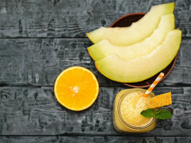 Smoothies de melão e fatias de melão em uma tigela de barro e laranja em uma mesa de madeira preta. a vista do topo. postura plana.