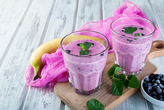 Smoothies de mirtilos e banana em copos e ingredientes em uma mesa de madeira