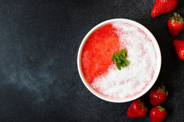 Smoothies de morango ou morangos com gelo em uma tigela branca. Servido com coco e hortelã. Uma bebida refrescante de verão. Fundo preto. Vista do topo. Copie o espaço