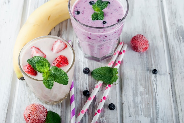 Smoothies de morangos, banana e mirtilos em copos e ingredientes em uma mesa de madeira