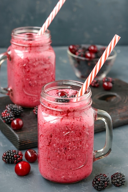 Smoothies mit Brombeeren und Kirschen im Glas auf dunkler Oberfläche, vertikale Ausrichtung, Nahaufnahme