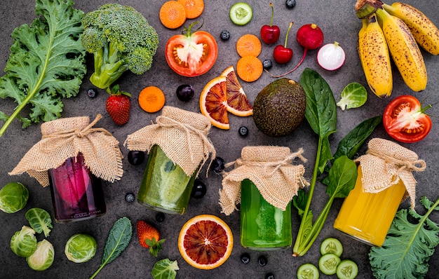 Foto smoothies saudáveis coloridos e sucos em garrafas com frutas tropicais e superalimentos na pedra escura